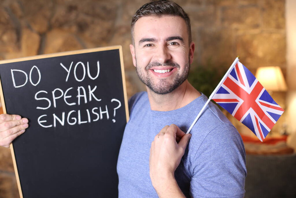 Портрет вродливого юнака, який тримає прапор Великої Британії та дошку, ви розмовляєте вдома англійською мовою. - Фото, зображення