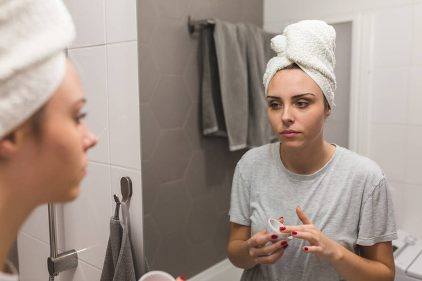 woman applying clay face mask in bathroom at her home - Фото, зображення