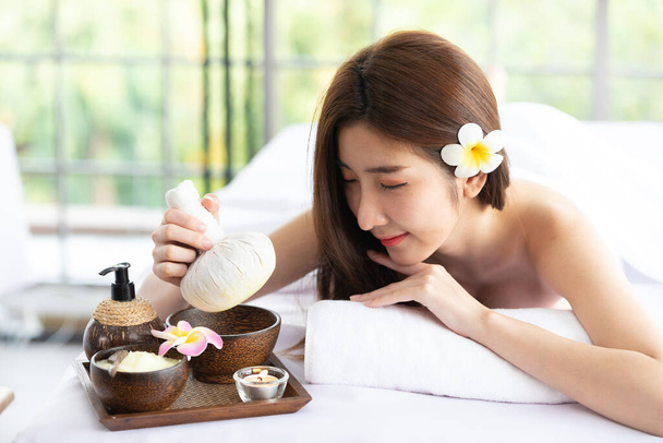 mooie aziatische vrouw houden en op zoek kruiden kompres ballen in spa salon - Foto, afbeelding