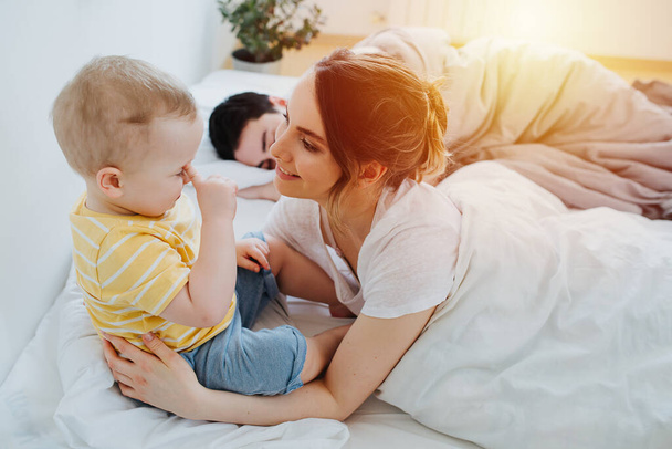 Mom talk with toddler in bed against the background of the father - Zdjęcie, obraz