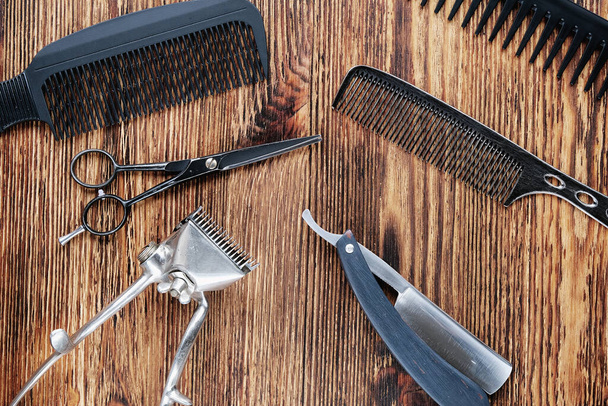 On a weathered wooden surface are old barber tools. Vintage manual hair clipper, combs, razor, hairdressing scissors. top view, flat lay. Barbershop background. horizontal orientation. - Фото, зображення