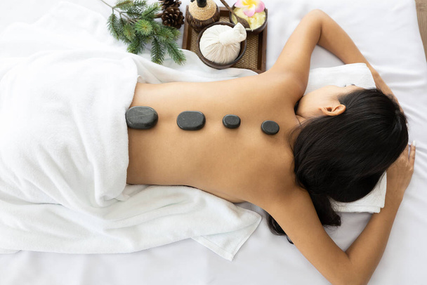 jonge aziatische vrouw slapen op bed voor massage in spa salon, met kruiden-apparatuur en spa stenen - Foto, afbeelding
