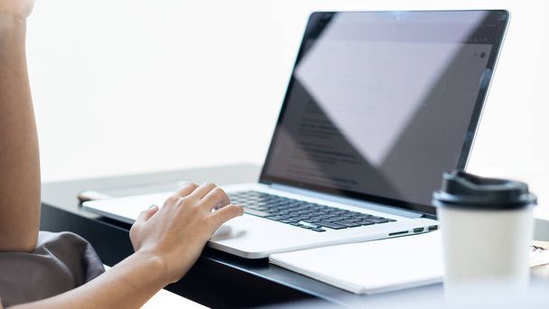 Рука деловой женщины, работающей на ноутбуке и кофейная кружка рядом с - Фото, изображение