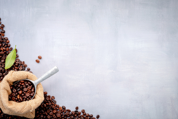Dunkle geröstete Kaffeebohnen in Hanfsäcken mit Schaufeln auf weißem Betonhintergrund. - Foto, Bild