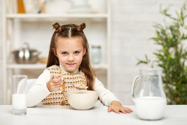 little girl eating breakfast: cereal with the milk in the kitchen. - Foto, afbeelding