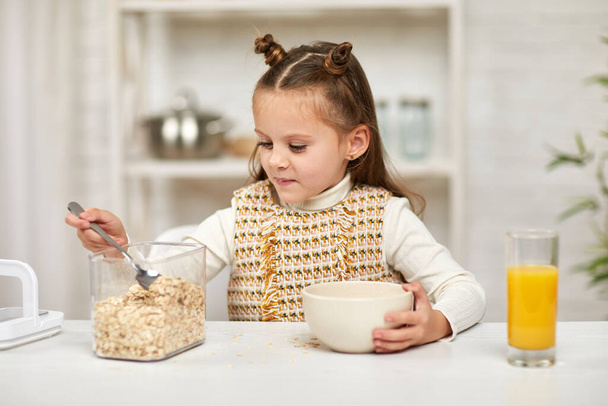 cute little girl eating breakfast: cereal and orange juice - Fotografie, Obrázek