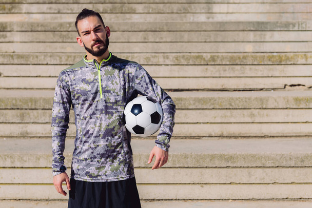 handsome sportsman in a concrete soccer court with the football ball under his arm, concept of healthy lifestyle and urban sport in the city, copy space for text - Foto, Bild