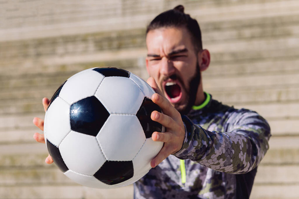 football ball in the hands of a sportsman screaming in a concrete soccer court, selective focus on the ball, concept of healthy lifestyle and urban sport in the city - Φωτογραφία, εικόνα