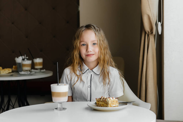 A cute little girl is sitting in a cafe and looking at a cake and cocoa close-up. Diet and proper nutrition - Foto, Imagem