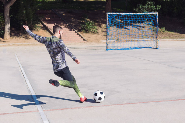 rear view of a football player kicking the soccer ball into an empty goal in a concrete football court, concept of healthy lifestyle and urban sport in the city, copy space for text - Photo, Image