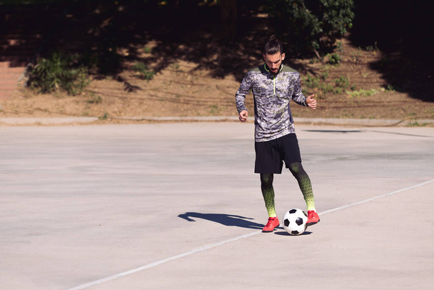 attractive sportsman playing the football ball in a concrete soccer court, concept of healthy lifestyle and urban sport in the city, copy space for text - Photo, Image