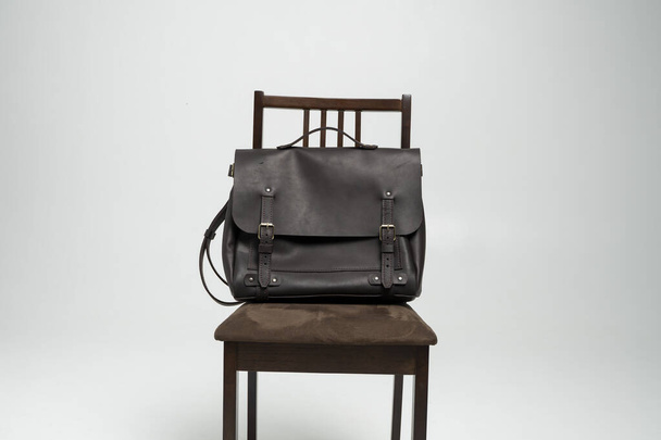 Brown mens shoulder leather bag for a documents and laptop on a brown chair with a white background. Mens leather brief case, messenger bags, leather satchel, handmade briefcase. - 写真・画像