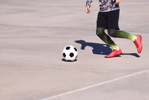 legs of an unrecognizable sportsman running with the ball in a concrete football court, concept of healthy lifestyle and urban sport in the city, copy space for text - Фото, зображення