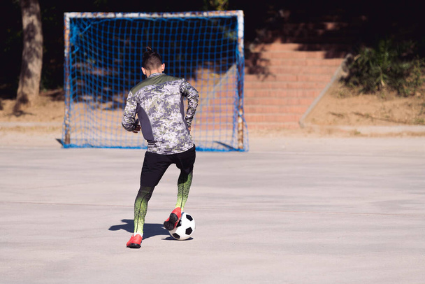rear view of an unrecognizable sportsman playing the soccer ball in a concrete football court with an empty goal, concept of healthy lifestyle and urban sport in the city, copy space for text - Photo, Image