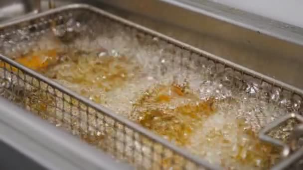 Le fette di patate rustiche stanno friggendo in olio bollente caldo a cucina. Croccanti patatine fritte stanno cuocendo in friggitrice. Processo di fabbricazione di fast food in cucina. Concetto di preparazione del cibo. Chiudere Lento mo - Filmati, video