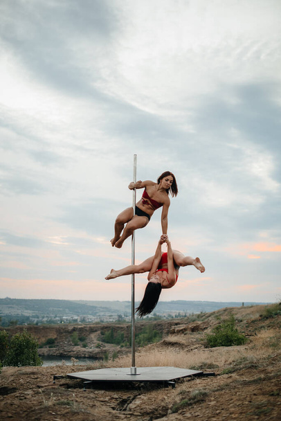 A young sexy girl performs amazing exercises on a pole during a beautiful sunset. Dance. Sexuality - Foto, afbeelding