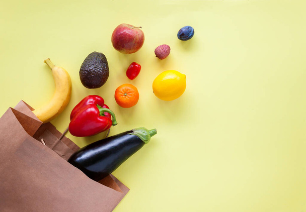 Shopping paper bag with different fruits and vegetables on a yellow background, flat lay. - Фото, зображення