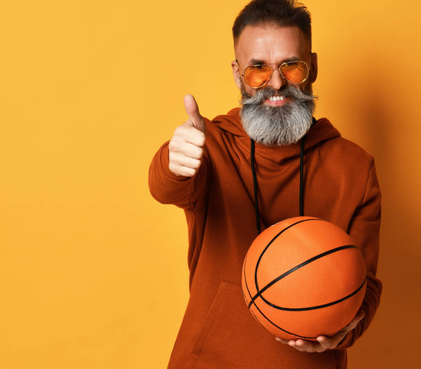 Smiling bearded man holding basket ball gesturing thumbs-up - Фото, зображення