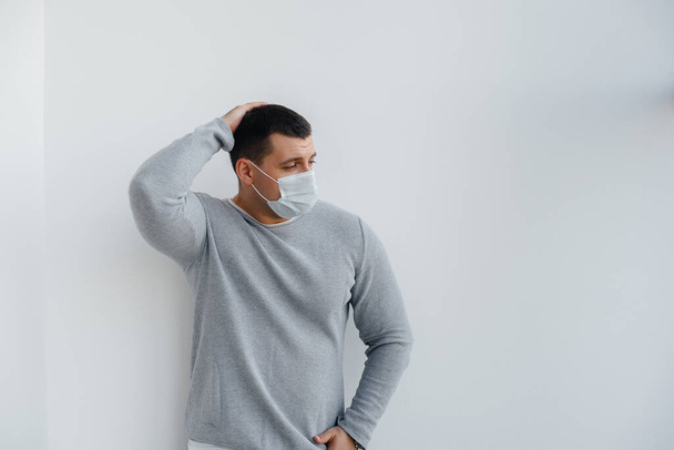 A young man stands on a gray background wearing a mask during a quarantine with free space. Quarantine in the mask - Fotografie, Obrázek