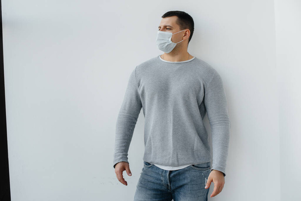 A young man stands on a gray background wearing a mask during a quarantine with free space. Quarantine in the mask - Φωτογραφία, εικόνα