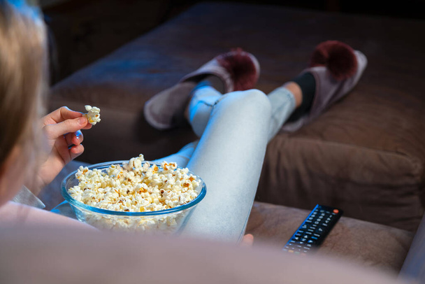 Close up of hand waking popcorn from a bowl while watching TV. Person sitting in comfortable couch and watching home cinema in the dark. - Fotoğraf, Görsel