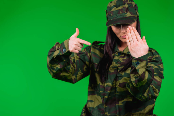 A married woman in a military uniform points with a forefinger to her hand with a wedding ring. Photo on a green background with side space - Fotó, kép