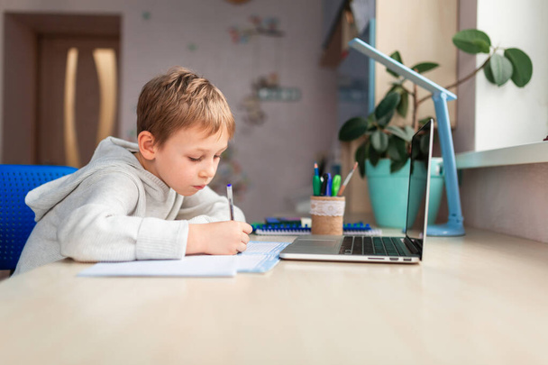 Cute little schoolboy studying at home doing school homework. Training books and notebook on the table. Distance learning online education - Fotoğraf, Görsel