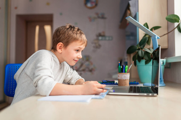 Cute little schoolboy studying at home doing school homework. Training books and notebook on the table. Distance learning online education - Foto, Imagen