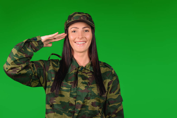 Portrait d'une femme militaire souriante caucasienne. Soldat saluant sur un fond vert avec un espace vide pour votre publicité - Photo, image