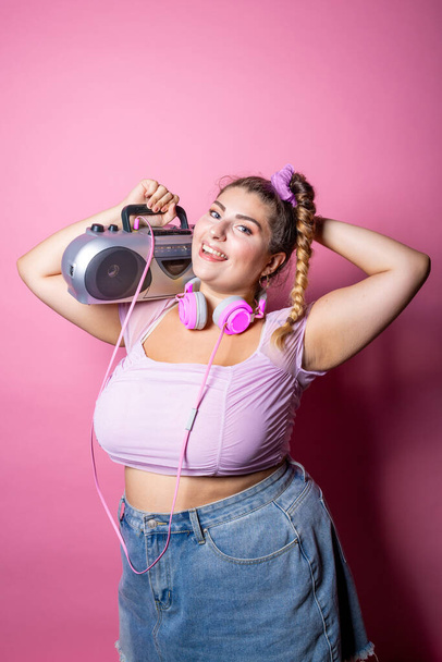 jong plus size mollige vrouw op roze achtergrond dansen holding stereo luisteren muziek geïsoleerde studio shot - genieten, diversiteit, lichaam positief concept - Foto, afbeelding
