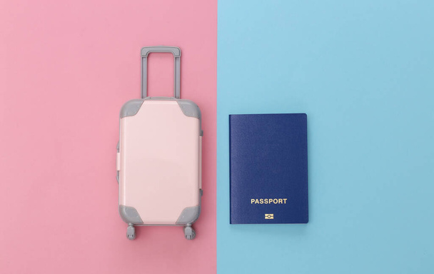 Utazási koncepció. Mini műanyag utazási táska és útlevél rózsaszín kék pasztell háttér. Minimális stílus. Felülnézet, lapos fektetés - Fotó, kép