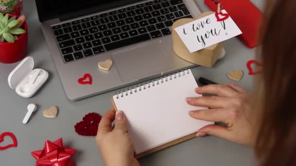 Alguien da la vuelta a la página de un cuaderno cerca de una tarjeta Te amo y la caja de regalo del día de San Valentín - Imágenes, Vídeo