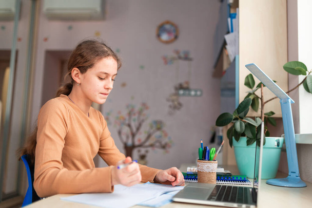 Beautiful schoolgirl studying at home doing school homework. Training books and notebook on the table. Distance learning online education - Foto, imagen