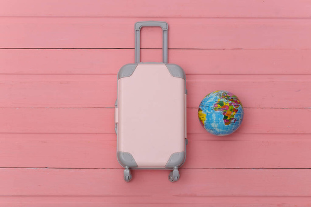 Piso laico vacaciones vacaciones y el concepto de planificación de viajes. Mini maleta de viaje de plástico y globo sobre fondo de madera rosa. Vista superior - Foto, imagen