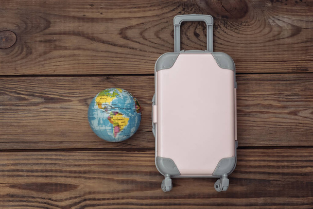 Piso laico vacaciones vacaciones y el concepto de planificación de viajes. Mini maleta de viaje de plástico y globo sobre fondo de madera. Vista superior - Foto, Imagen