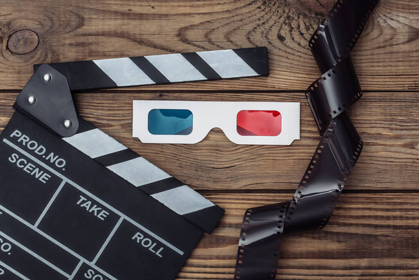 木製の背景にフィルムテープと3Dメガネとフィルムクラッパーボード。映画業界、エンターテイメント。トップ表示 - 写真・画像