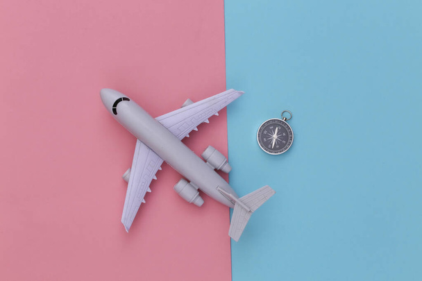 Minimalizm podróżuje płasko. Kompas i samolot na niebiesko-różowym pastelowym tle. Widok z góry - Zdjęcie, obraz