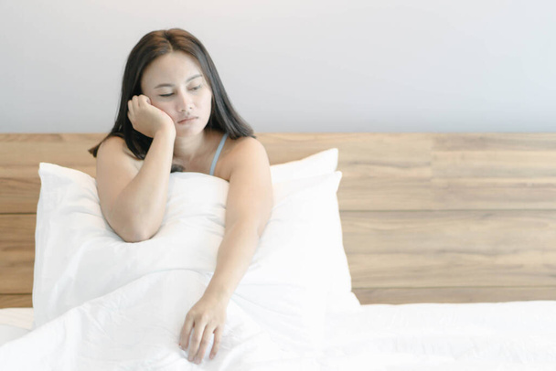 Gros plan femme assise sur le lit dans la chambre à coucher avec la pensée ou le sentiment déprimé, foyer sélectif - Photo, image