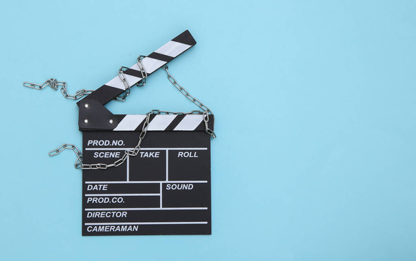 Movie clapperboard wrapped in steel chain on blue background. Ban on filmmaking. Top view - Photo, Image