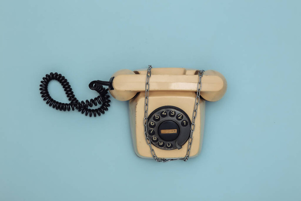 Περιστροφικό τηλέφωνο τυλιγμένο σε ατσάλινη αλυσίδα σε μπλε φόντο. Άνω όψη - Φωτογραφία, εικόνα