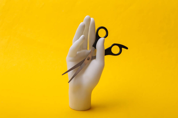 Рука манекена держит ножницы для волос на желтом фоне. Концепция минимализма - Фото, изображение