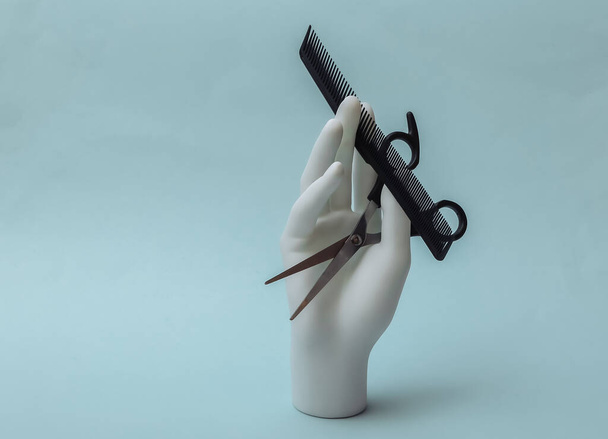Mannequin mano sosteniendo tijeras para el cabello y peine sobre fondo azul. Concepto de belleza minimalista - Foto, Imagen