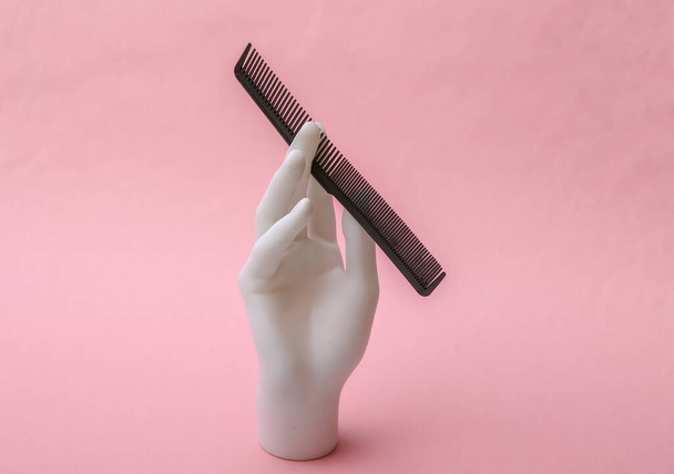 Mannequin hand holding comb on pink background. Minimalism beauty concept - Foto, Imagen