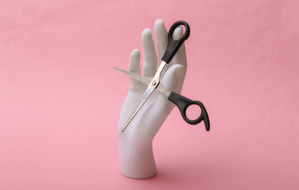Μανεκέν χέρι κρατώντας ψαλίδι μαλλιών σε ροζ φόντο. Minimalism έννοια ομορφιά - Φωτογραφία, εικόνα
