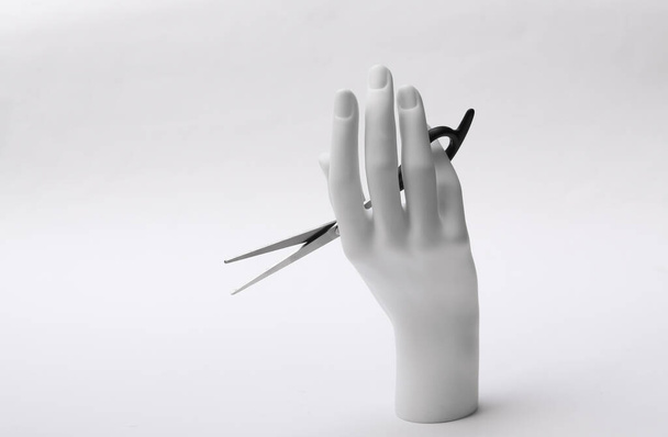 Рука манекена держит ножницы для волос на белом фоне. Концепция минимализма - Фото, изображение