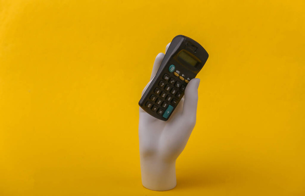 Белый манекен рука держит калькулятор на желтом фоне. - Фото, изображение