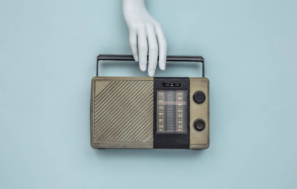 Die weiße Hand der Schaufensterpuppe hält einen Retro-Radioempfänger auf blauem Hintergrund. Ansicht von oben - Foto, Bild