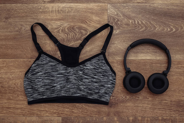 Sports top bra and stereo headphones on wooden background. Sport and fitness. Getting ready for training. Top view. Flat lay - Photo, Image