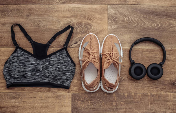 Sports shoes, top bra and stereo headphones on wooden background. Getting ready for training. Top view. Flat lay - Photo, Image