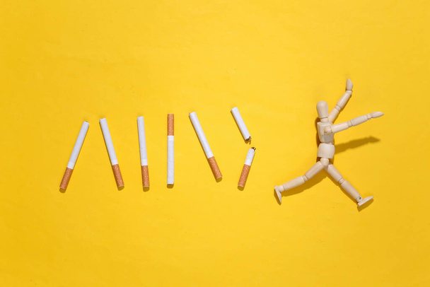 Wooden puppet runs from cigarettes on a yellow background. Quitting smoking concept - Photo, Image